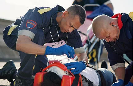 Emergency responders provide medical assistance to an injured person lying on the ground with a neck brace and medical equipment nearby