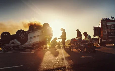 Emergency responders assisting victims at the scene of a car crash with overturned vehicle at sunset