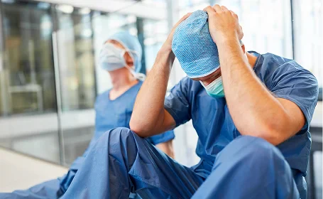 Stressed medical professionals sitting on the floor in hospital, showing emotional exhaustion