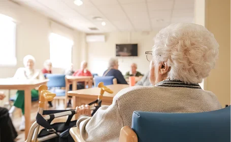 Elderly woman in wheelchair at a senior care home with other residents in background