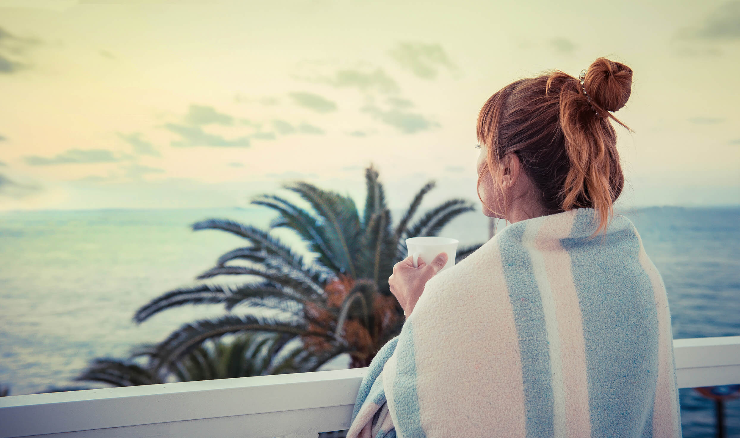 Woman with mug wrapped in Blanket looking at ocean